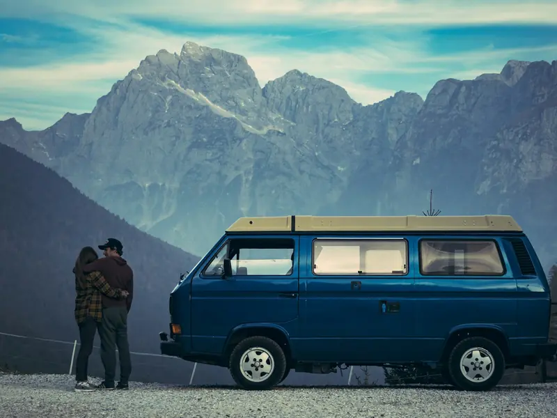 Van aménagé stationné face aux sommets enneigés des Alpes françaises avec lac de montagne