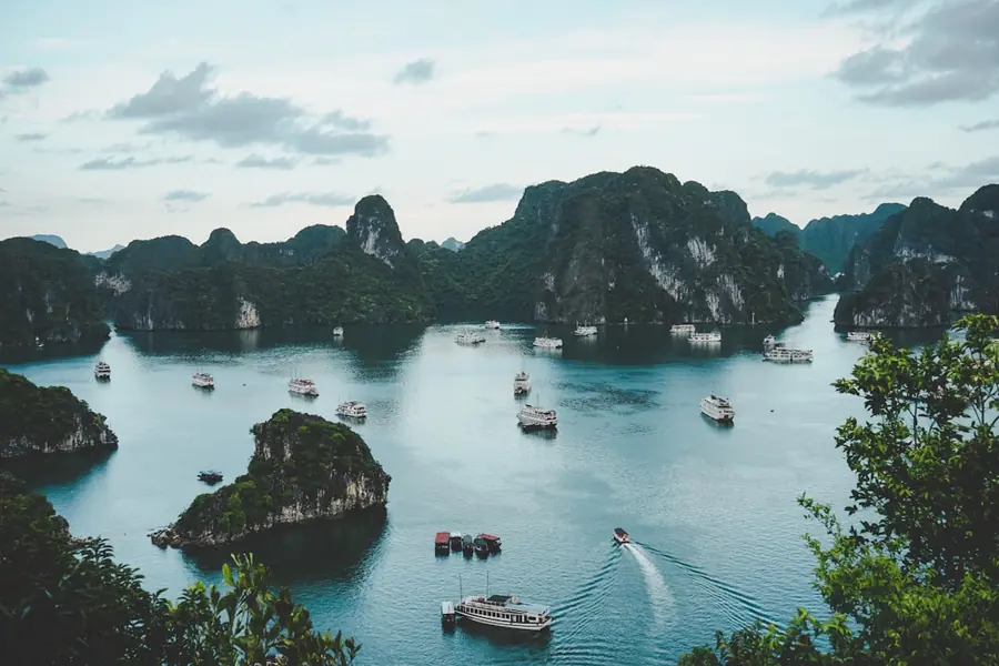 Baie d'Halong avec jonques traditionnelles naviguant entre les îlots karstiques au coucher du soleil